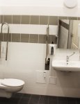 Toaleta w Dziennym Domu Pomocy. Kremowo brązowe płytki ceramiczne. Na ścianie umywalka z lustrem